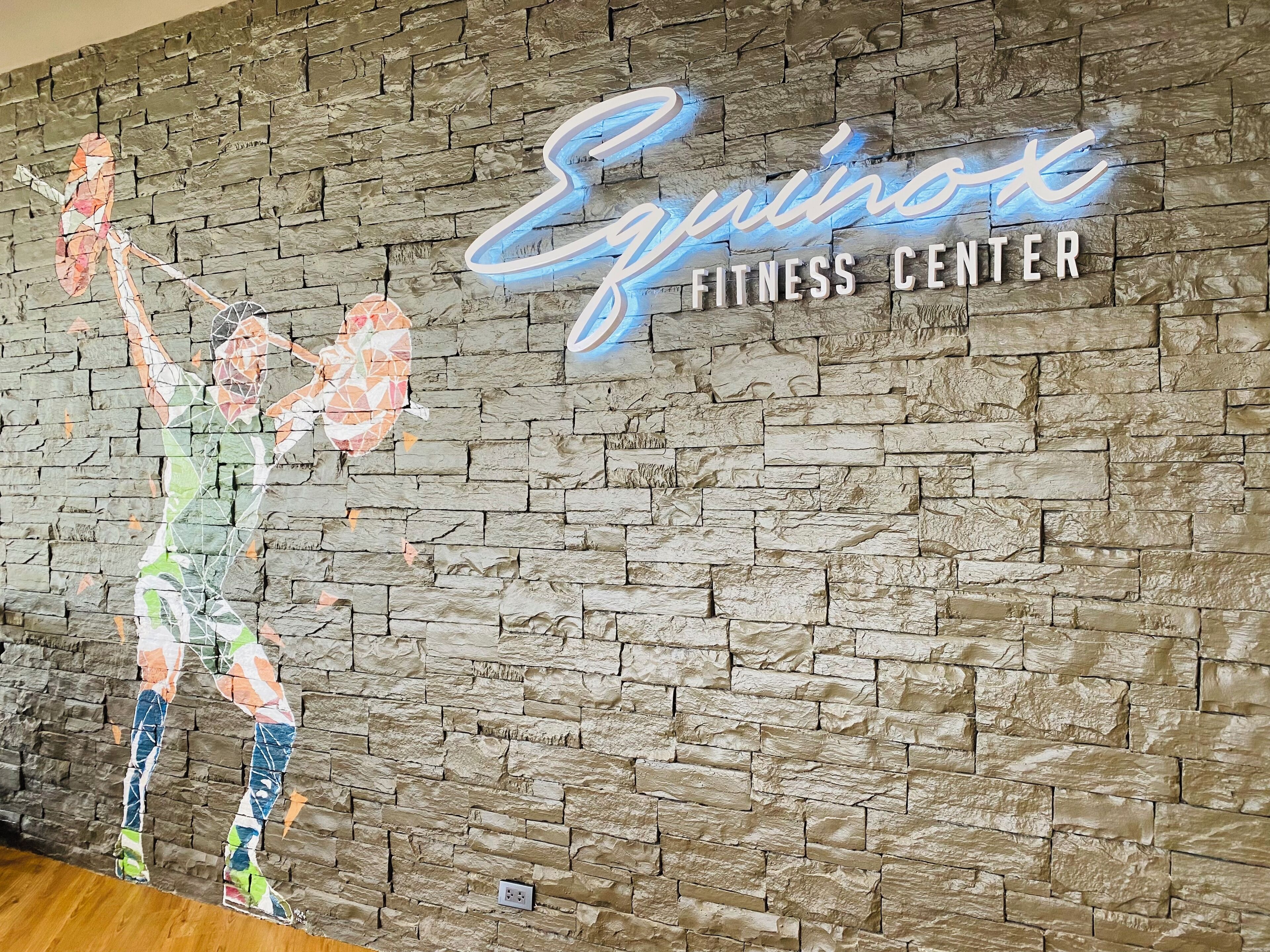 A wall with a mosaic of a person lifting weights and the text "Equinox Fitness Center".