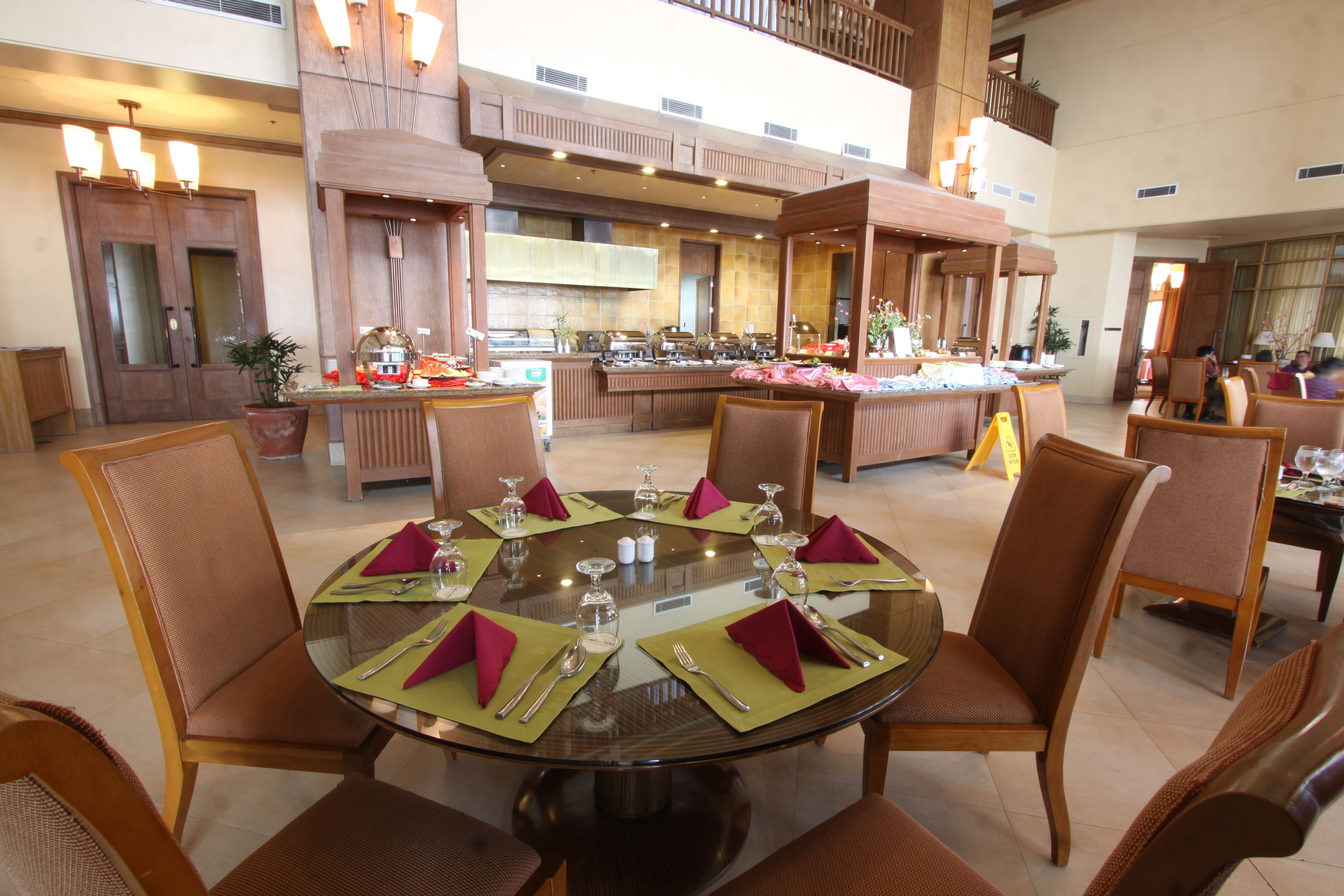 A spacious dining area with a high ceiling, multiple dining tables set with green placemats and red napkins, and wooden chairs.
