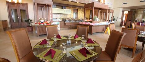 A spacious dining area with a high ceiling, multiple dining tables set with green placemats and red napkins, and wooden chairs.