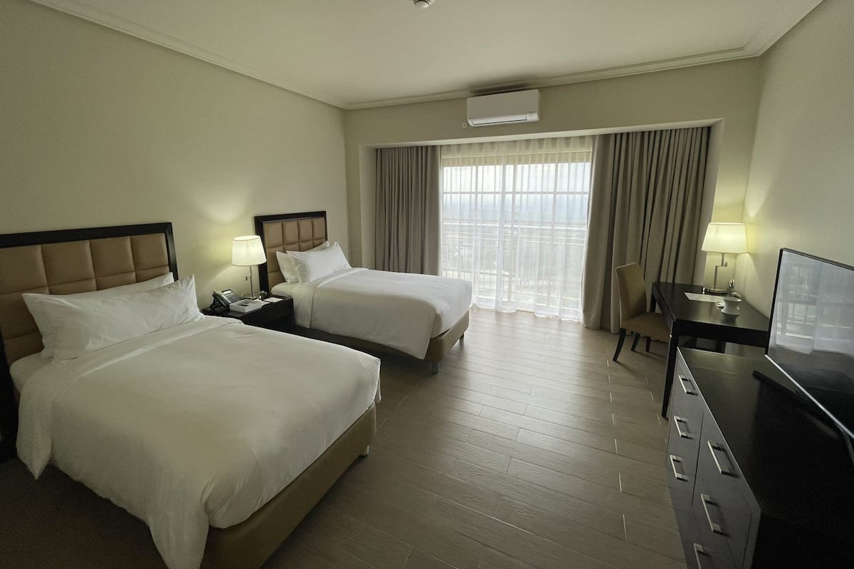 A hotel room with two beds, a desk, a chair, and a television.
