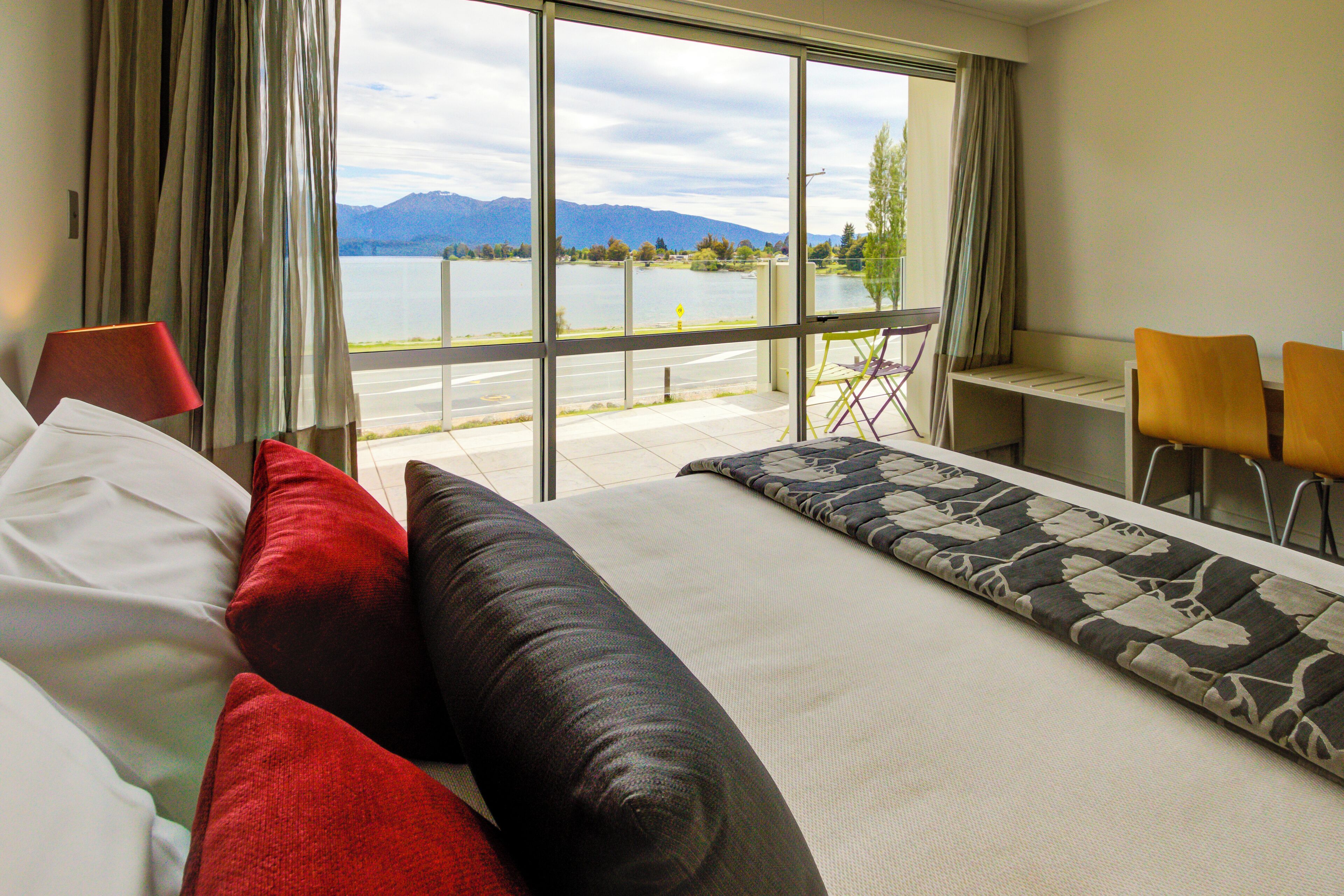 Habitación de hotel con cama, escritorio y vista a un lago y montañas.