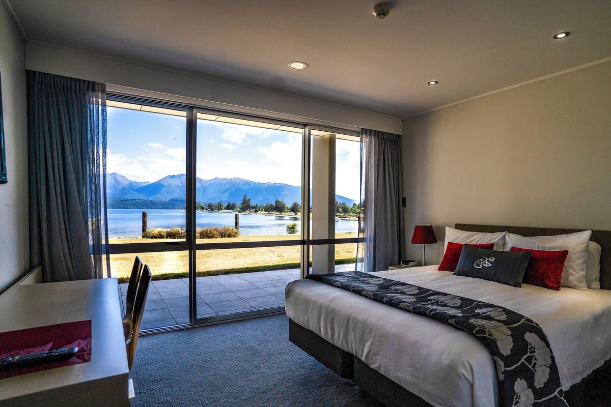 A hotel room with a large bed, a desk, and a view of mountains and a lake.
