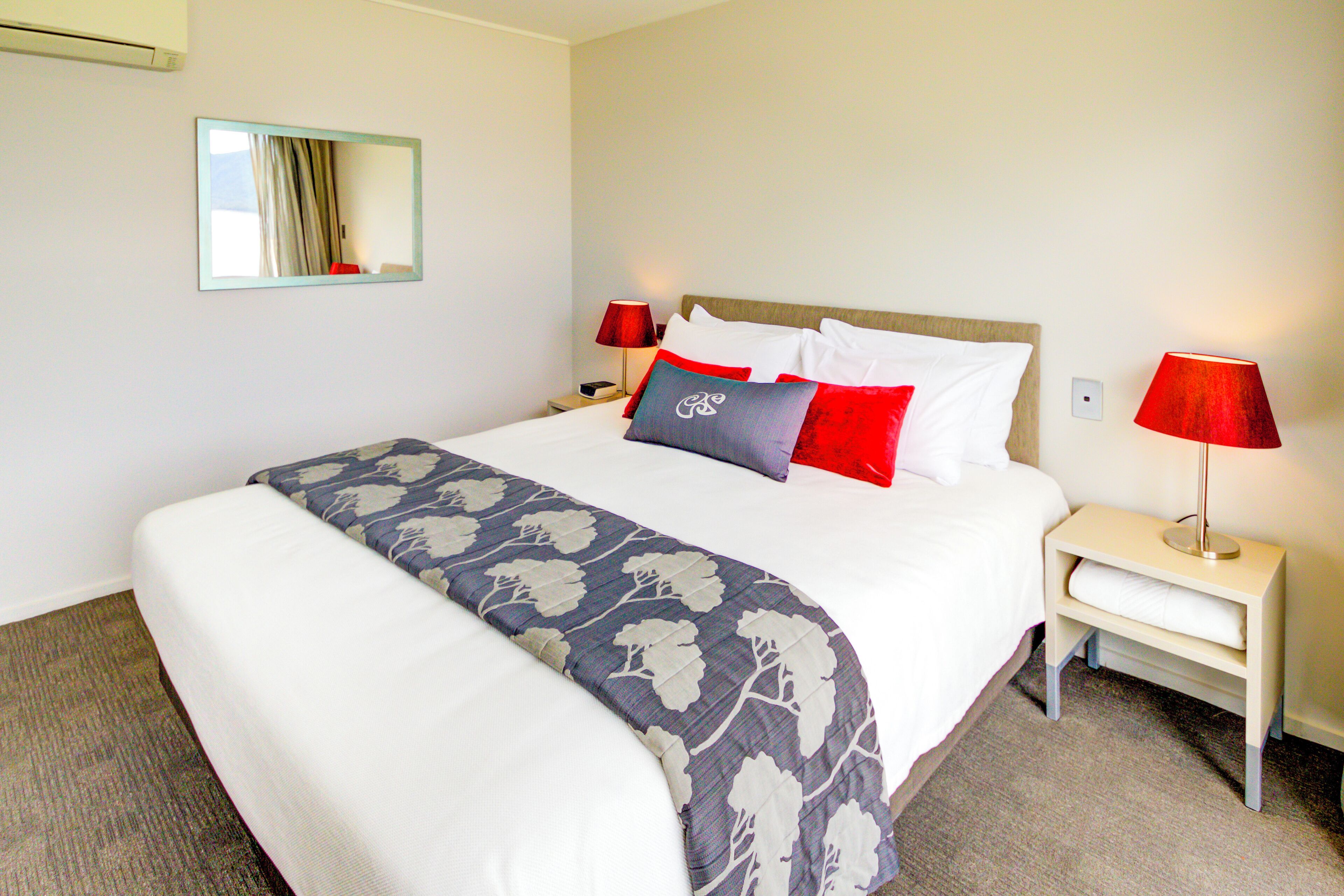 A neatly made bed with a floral-patterned bedspread, two bedside tables with lamps, and a mirror on the wall.