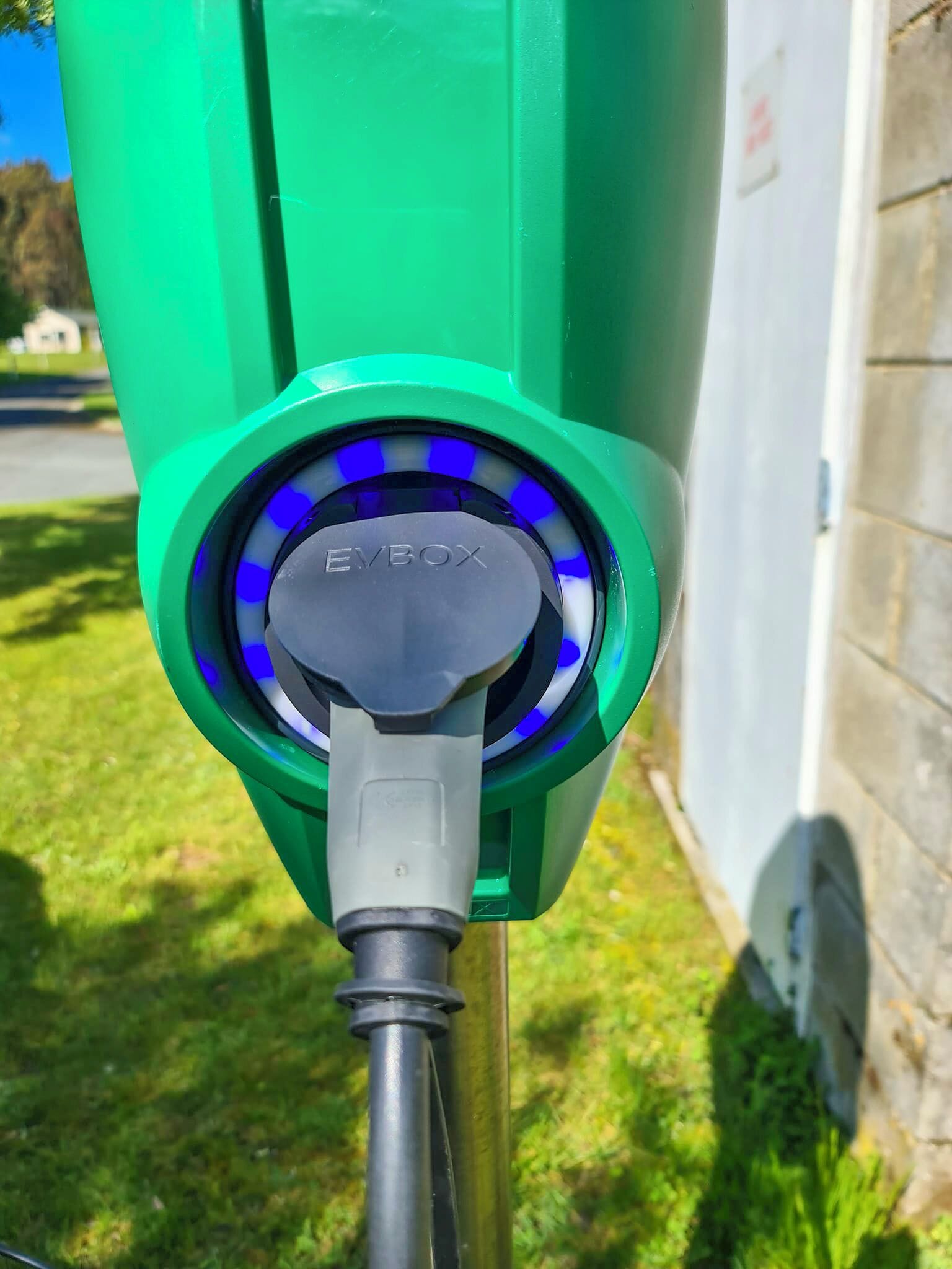 Una estación de carga para vehículos eléctricos verde, con el nombre de la marca a la vista y un cable de carga conectado.