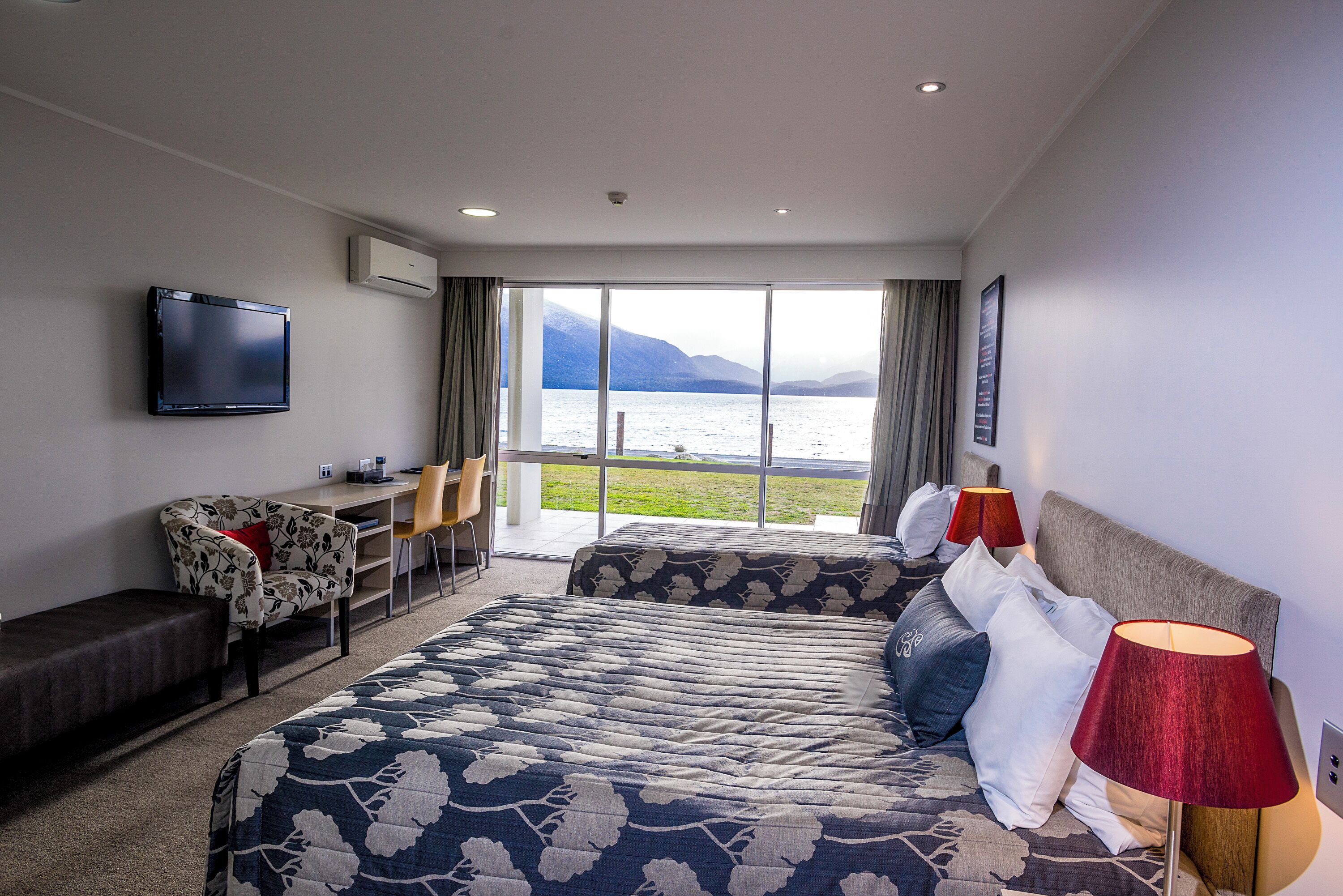 A hotel room with a bed, a desk, a chair, a TV, and a view of the water.