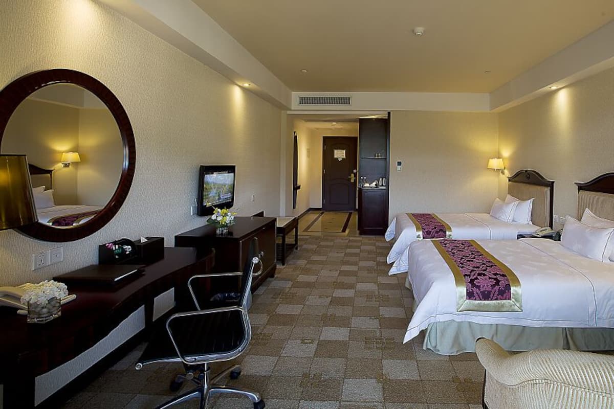 Une chambre d’hôtel avec deux lits, un bureau avec une chaise, un grand miroir et un téléviseur.