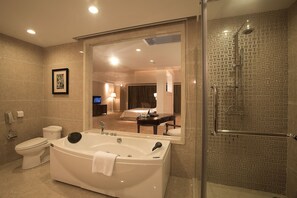 A modern bathroom with a large bathtub, a glass-enclosed shower, and a visible bedroom with a TV and a desk. - Country Garden Phoenix Hot Spring Hotel Xianning (Xianning)