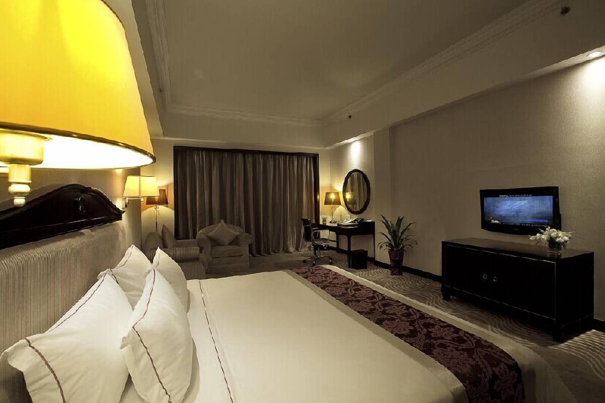 Une chambre d’hôtel avec un grand lit, un bureau avec une chaise, une télévision et une lampe.