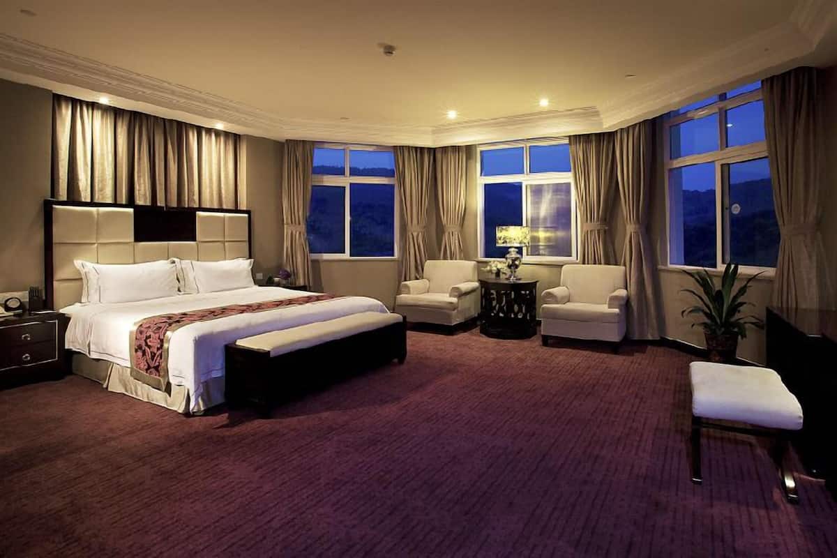 Une chambre d’hôtel avec un grand lit, deux fauteuils, une petite table, un téléviseur et une fenêtre avec des rideaux.