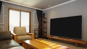 A living room with a sofa, armchair, wooden coffee table, TV, and a small shelf. - Ariana Hotel (Daegu)