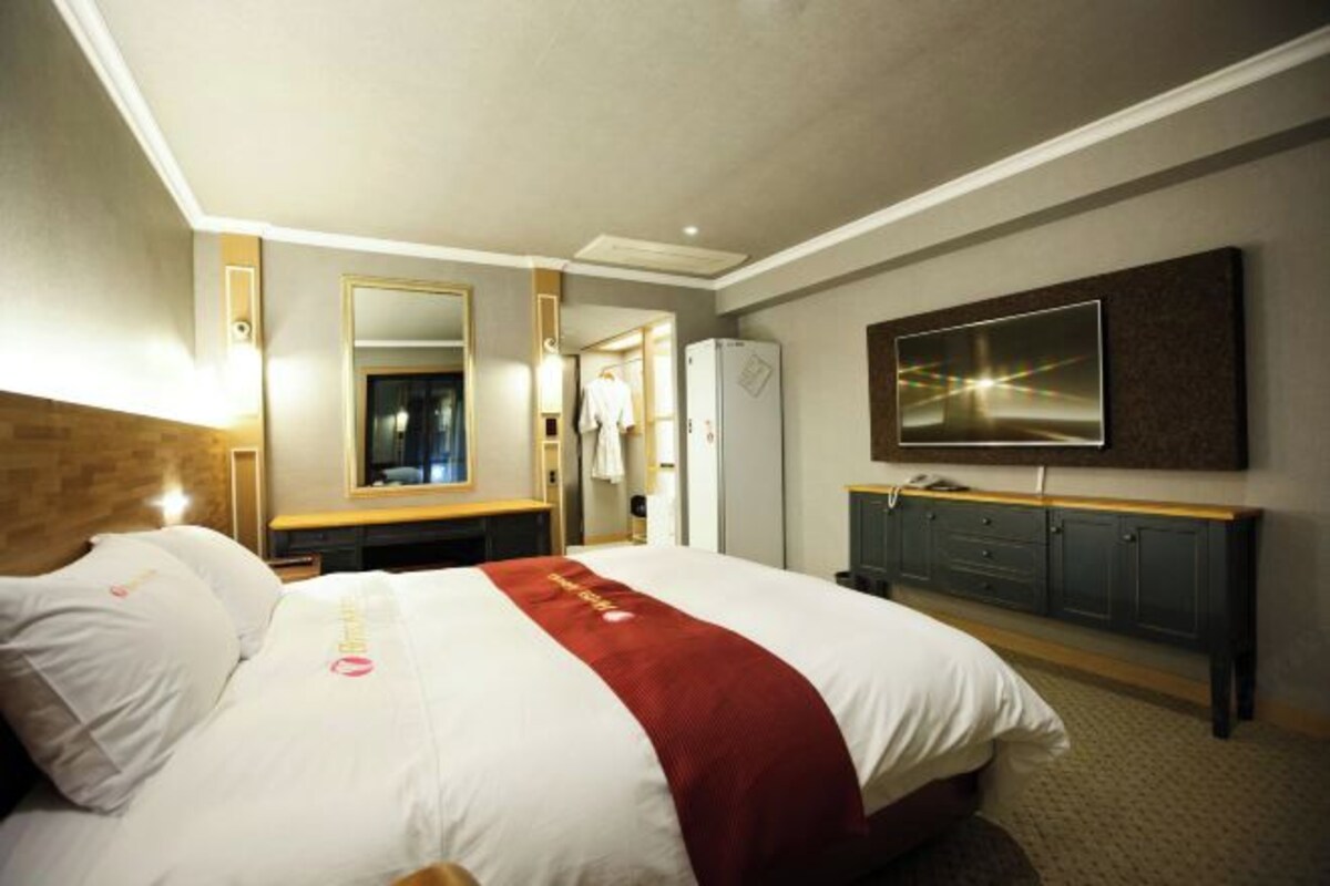 Ett hotellrum med en stor säng, en tv som är monterad på väggen, en spegel och en byrå i trä.