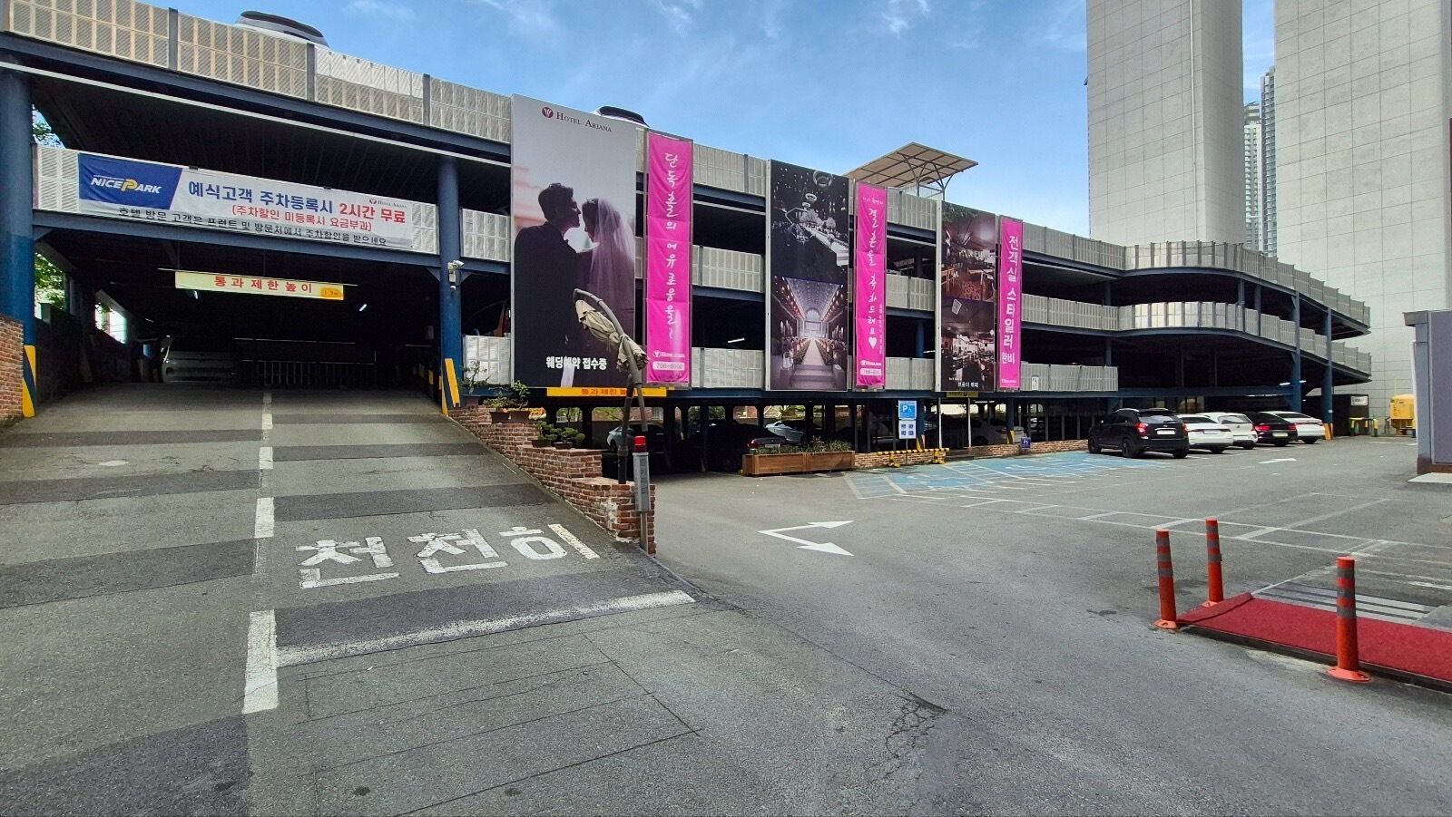 A multi-level parking structure with a hotel entrance, marked pedestrian crossing, and directional arrows on the pavement.