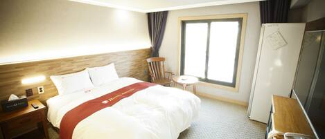 Una habitación de hotel con cama, mesita de noche, silla, escritorio y ventana.