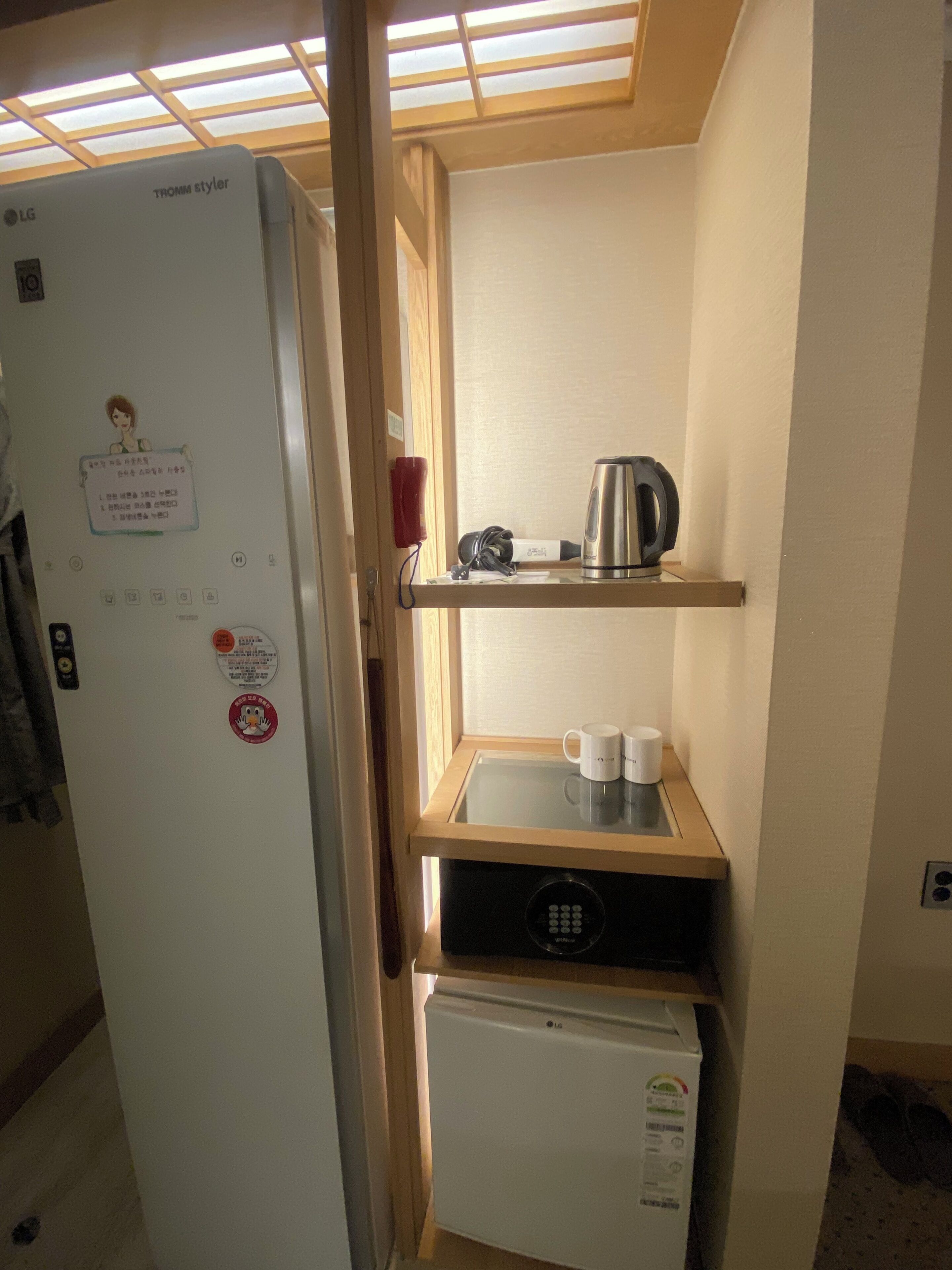 Una cucina compatta con frigorifero, microonde ed uno scaffale con bollitore e tazze.