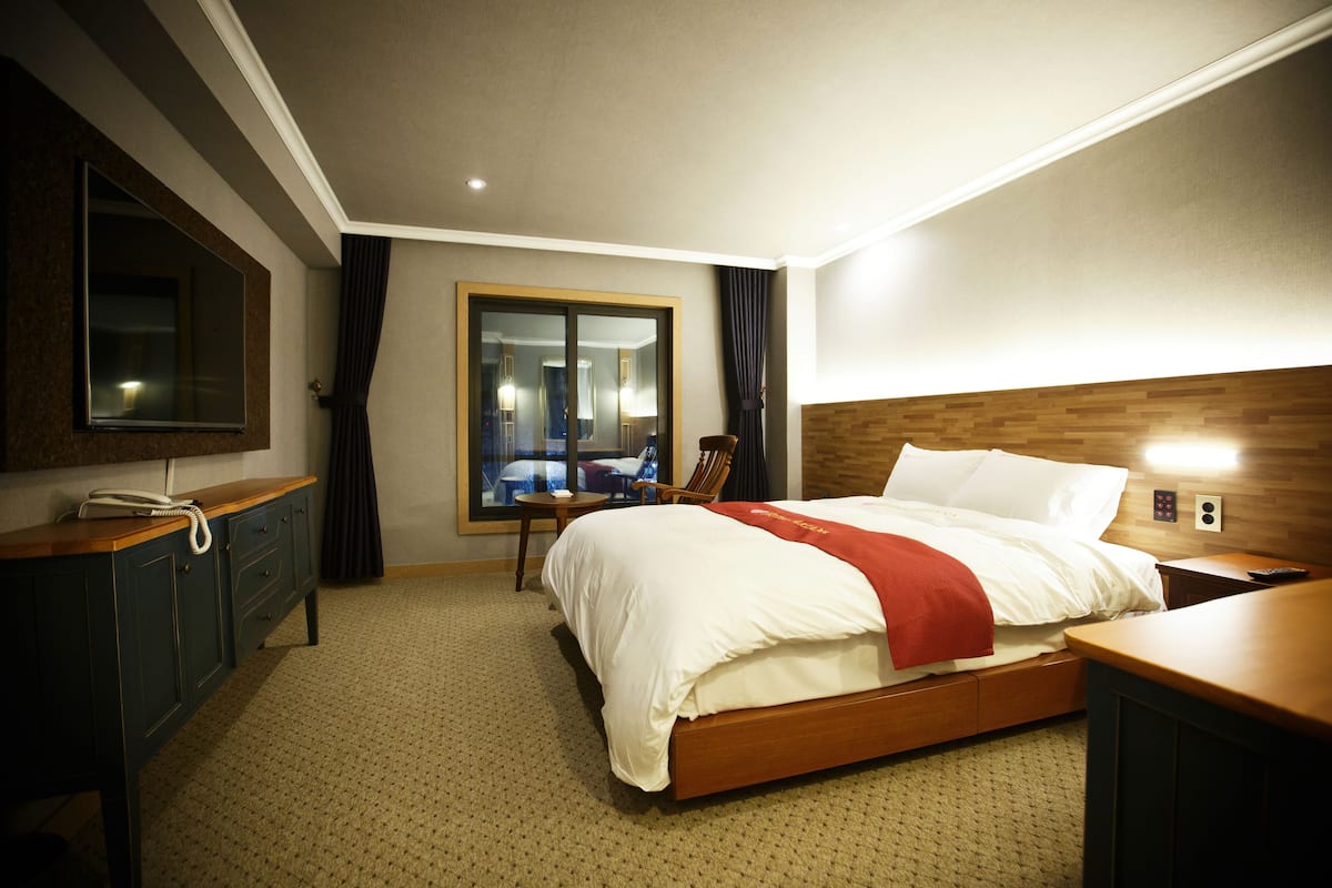 A hotel room with a large bed, a desk, a chair, a mirror, and a window with curtains.