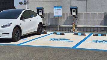 A white car parked in a designated electric vehicle charging station with a blue parking sign and a charging box.