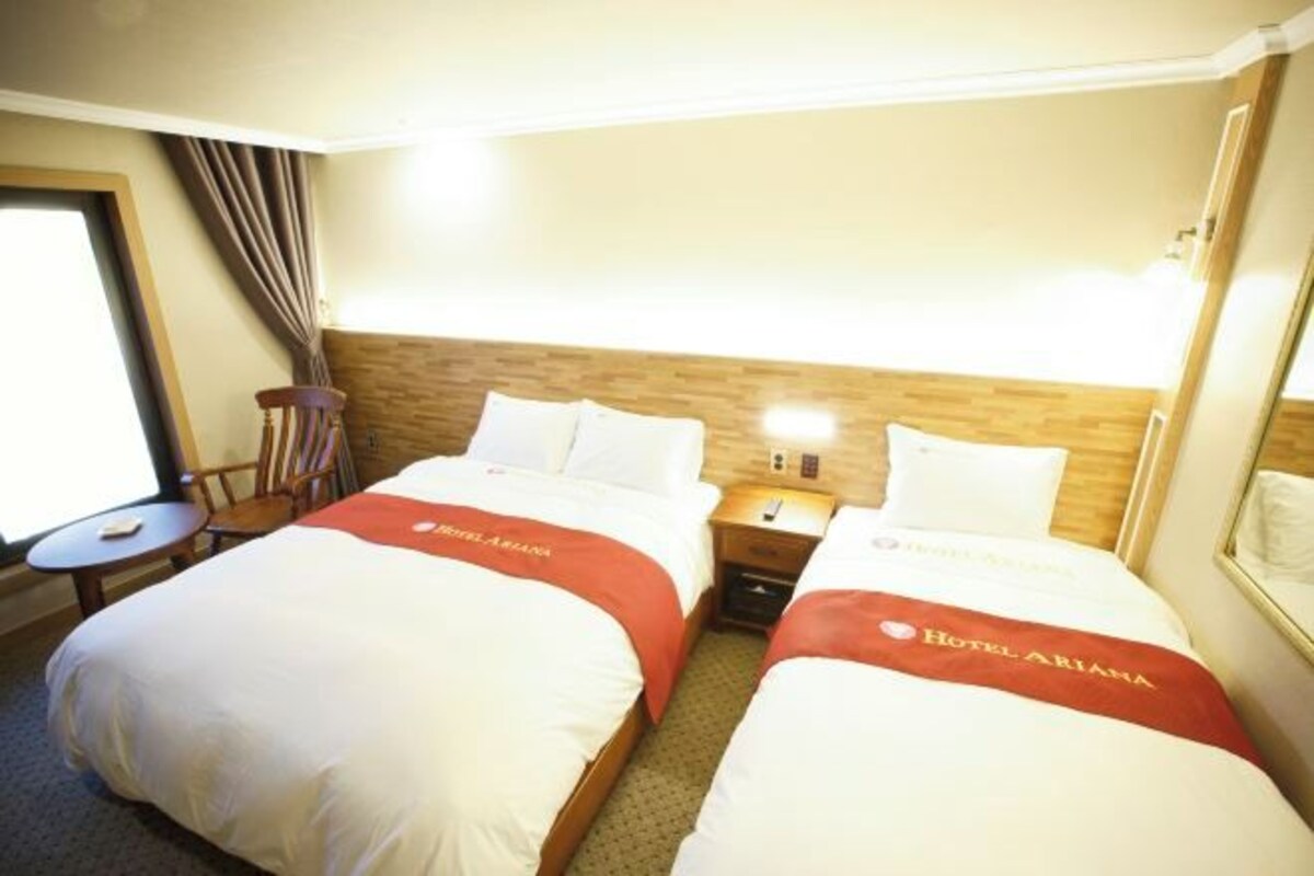 Ett hotellrum med två sängar, ett nattduksbord, en stol, ett litet bord och ett fönster med gardiner.