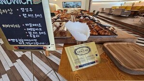 A sandwich counter with a menu board, a tray of pastries, and a certificate on a table. - Ariana Hotel (Daegu)