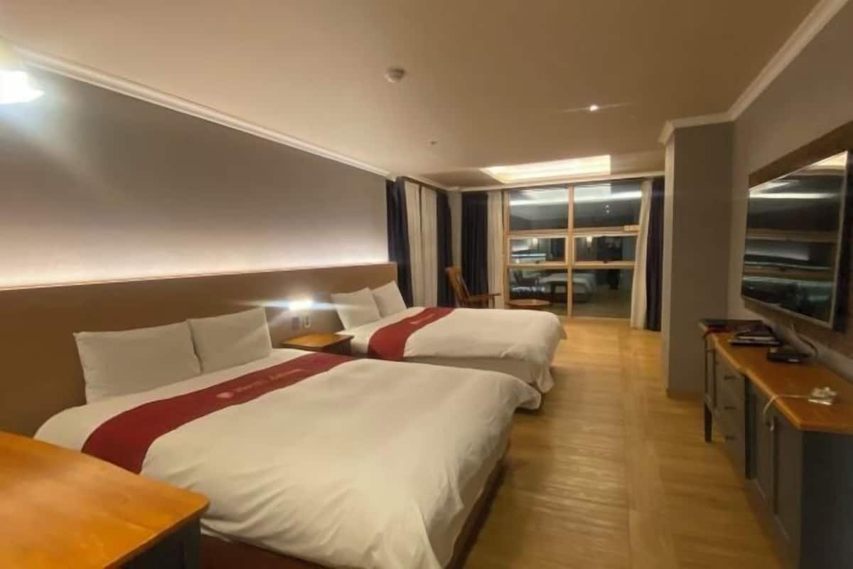 A hotel room with two beds, a TV, a desk, and a large window.