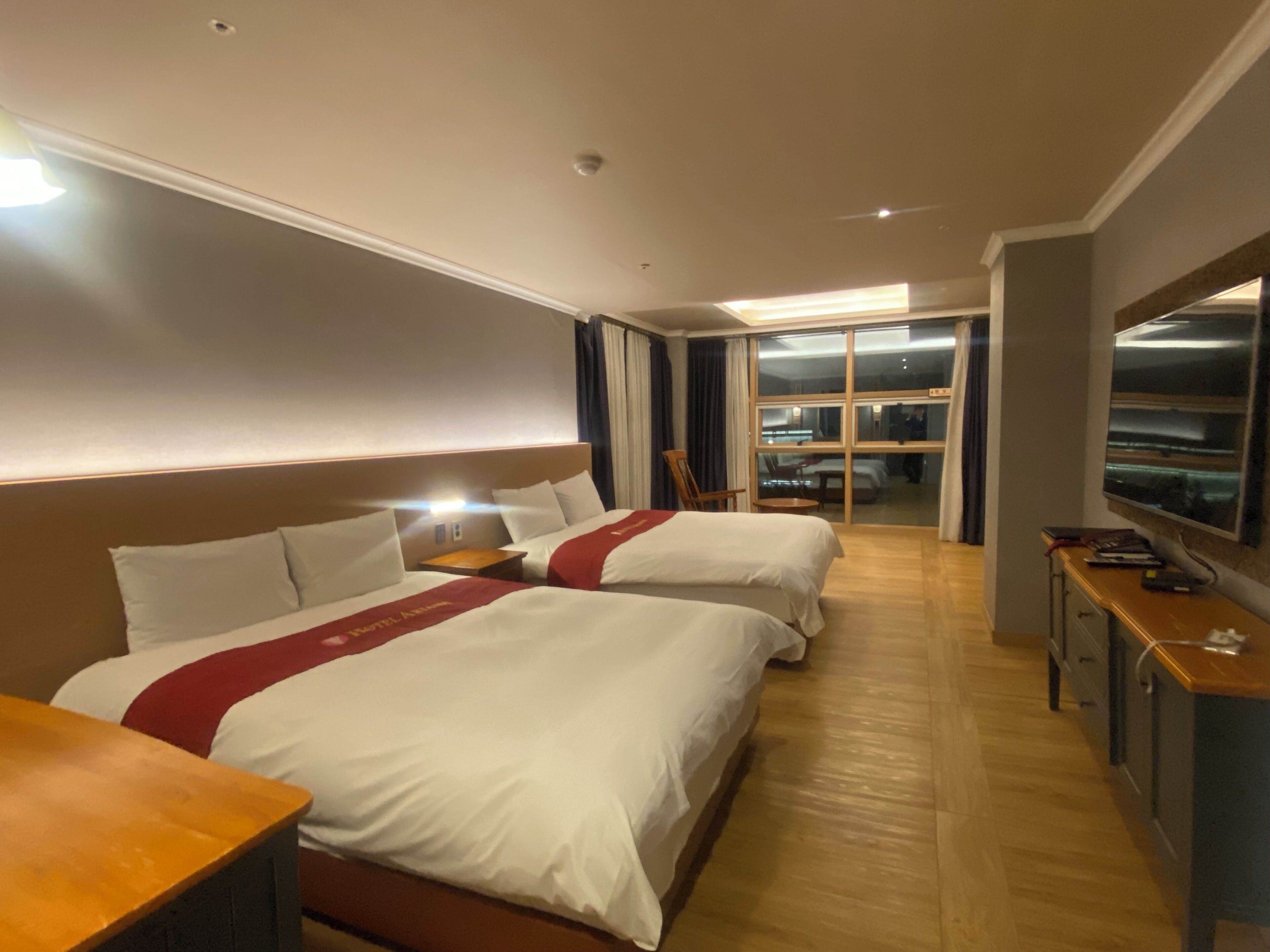 A hotel room with two beds, a desk, a TV, and a sliding door leading to a balcony.