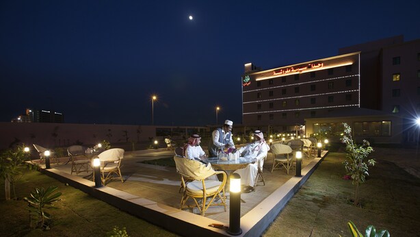 An outdoor dining area with tables and chairs, illuminated by ground lights, in front of a hotel building with illuminated signage. - Palms Lily Hotel Suites (Al-Hofuf)