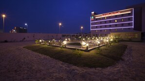 A hotel with a well-lit outdoor area featuring multiple lounge chairs and tables, a swimming pool, and a building with illuminated signage. - Palms Lily Hotel Suites (Al-Hofuf)