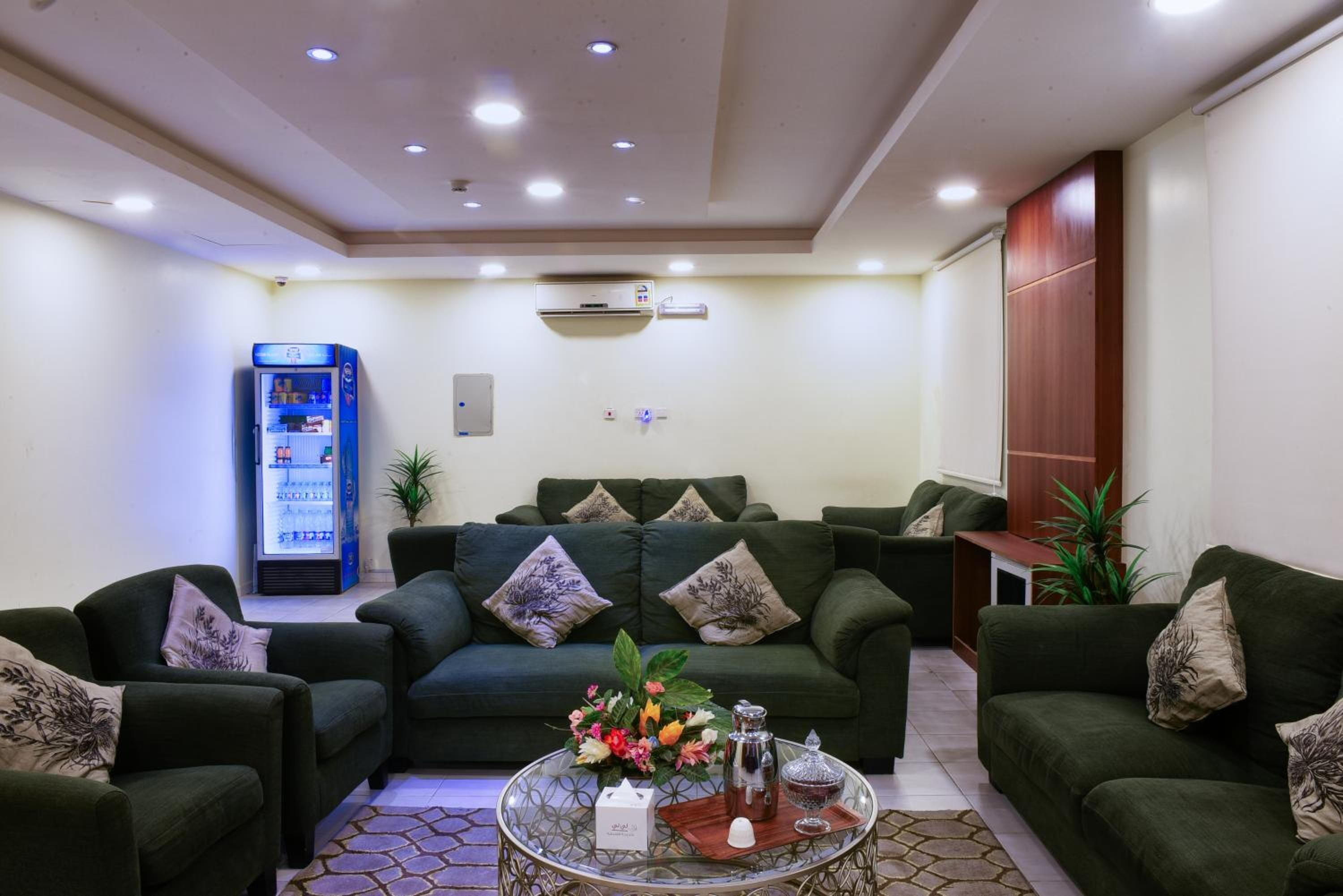 Un salón moderno con sofás verdes, una mesa de centro con objetos decorativos y una máquina expendedora azul.