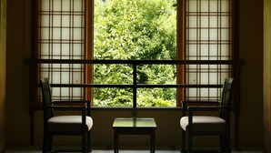 Um quarto com uma janela tradicional em estilo japonês, duas cadeiras e uma mesa pequena.