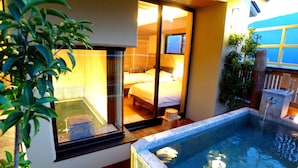 Uma banheira de hidromassagem com um deck de madeira, uma sala envidraçada com uma cama e uma mesa pequena com uma toalha.
