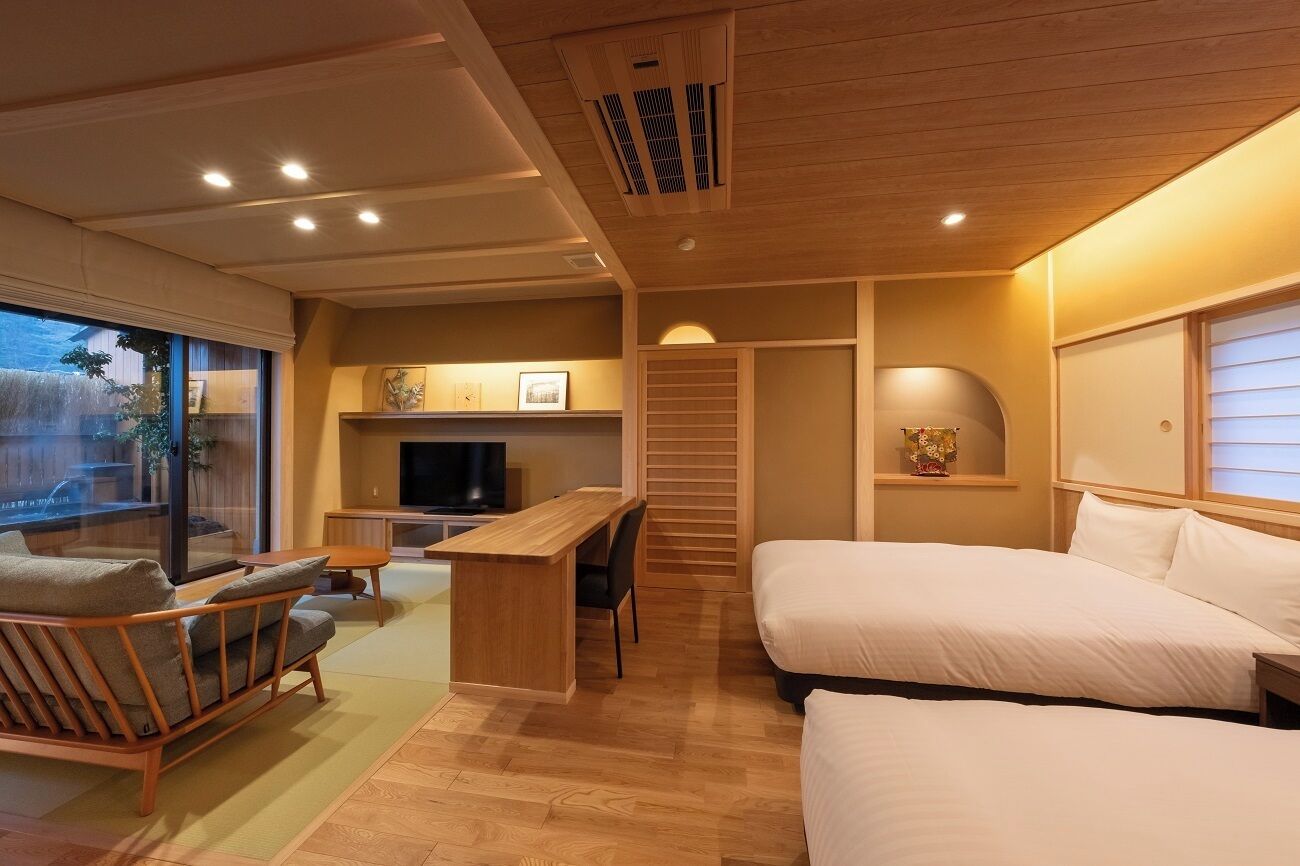 A modern hotel room with a wooden ceiling, a sofa, a desk, a TV, and a bed.