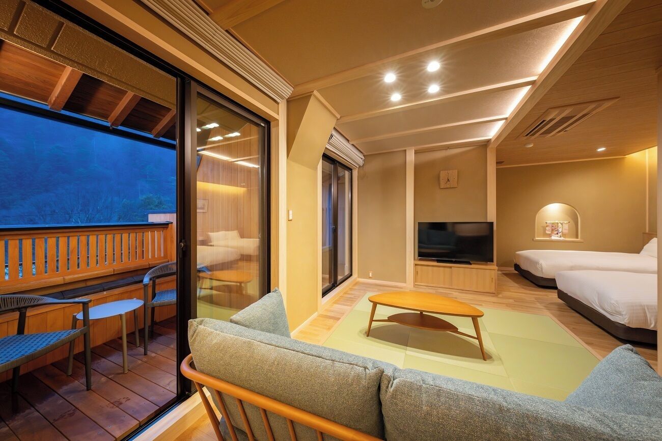 A modern hotel room with a balcony, a TV, a sofa, and a bed.