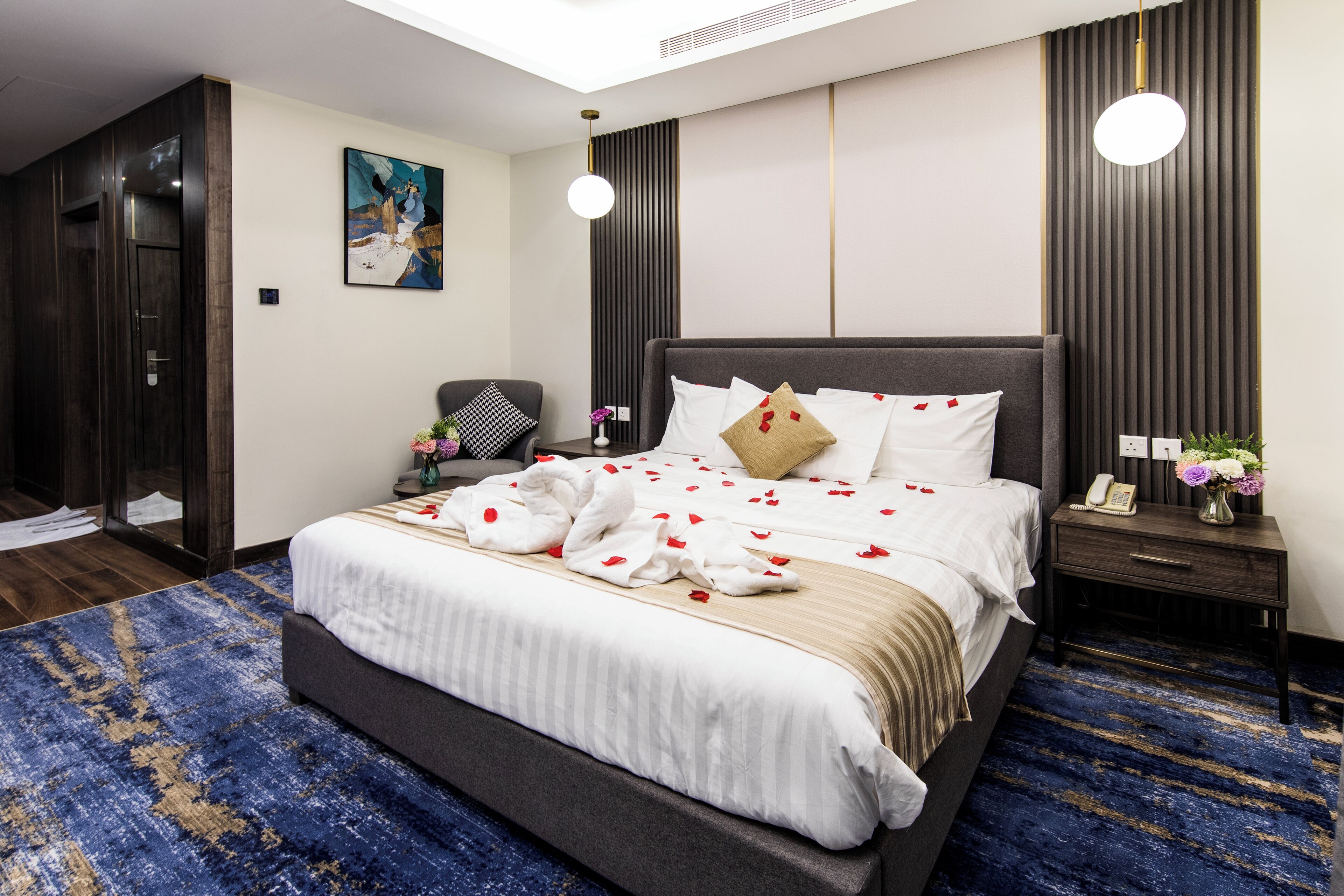 Een moderne hotelkamer met een groot bed, een nachtkastje met een lamp, een schilderij aan de muur en een donker houten kledingkast.