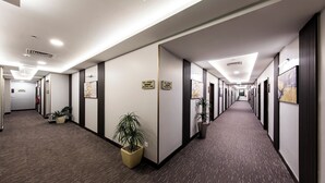 A long, narrow hallway with office cubicles on both sides, potted plants, and signs indicating directions. - Lily Hotel Suite Hofuf (Al-Hofuf)