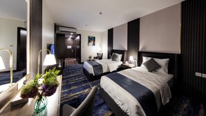 A hotel room with two beds, a desk with a lamp, a vase of flowers, and a large mirror. - Lily Hotel Suite Hofuf (Al-Hofuf)