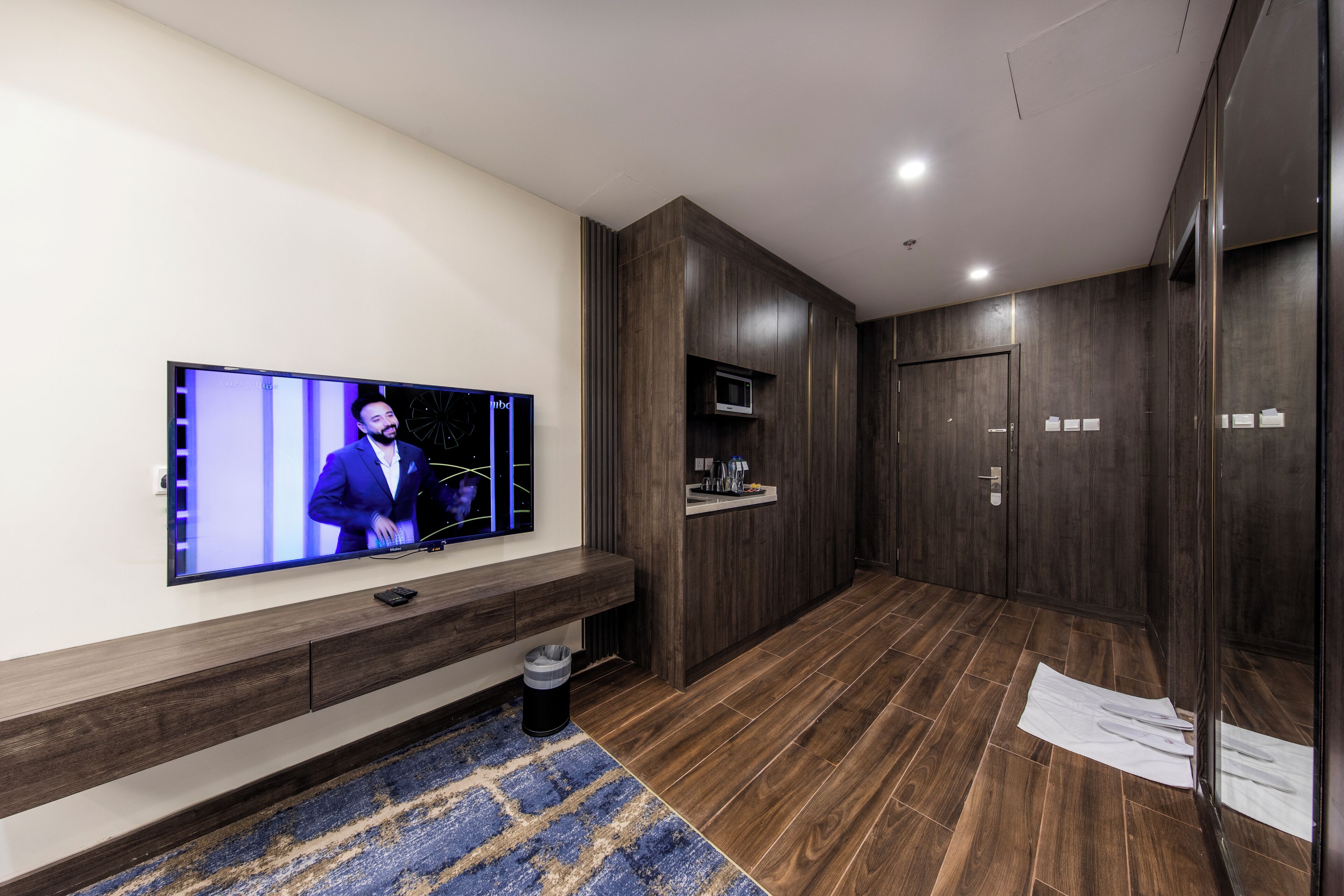 Een moderne hotel lobby met een flatscreen televisie, een houten bank, een prullenbak en een magnetron.
