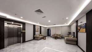 A modern lobby with a marble floor, two sofas, a coffee table, and an elevator. - Lily Hotel Suite Hofuf (Al-Hofuf)