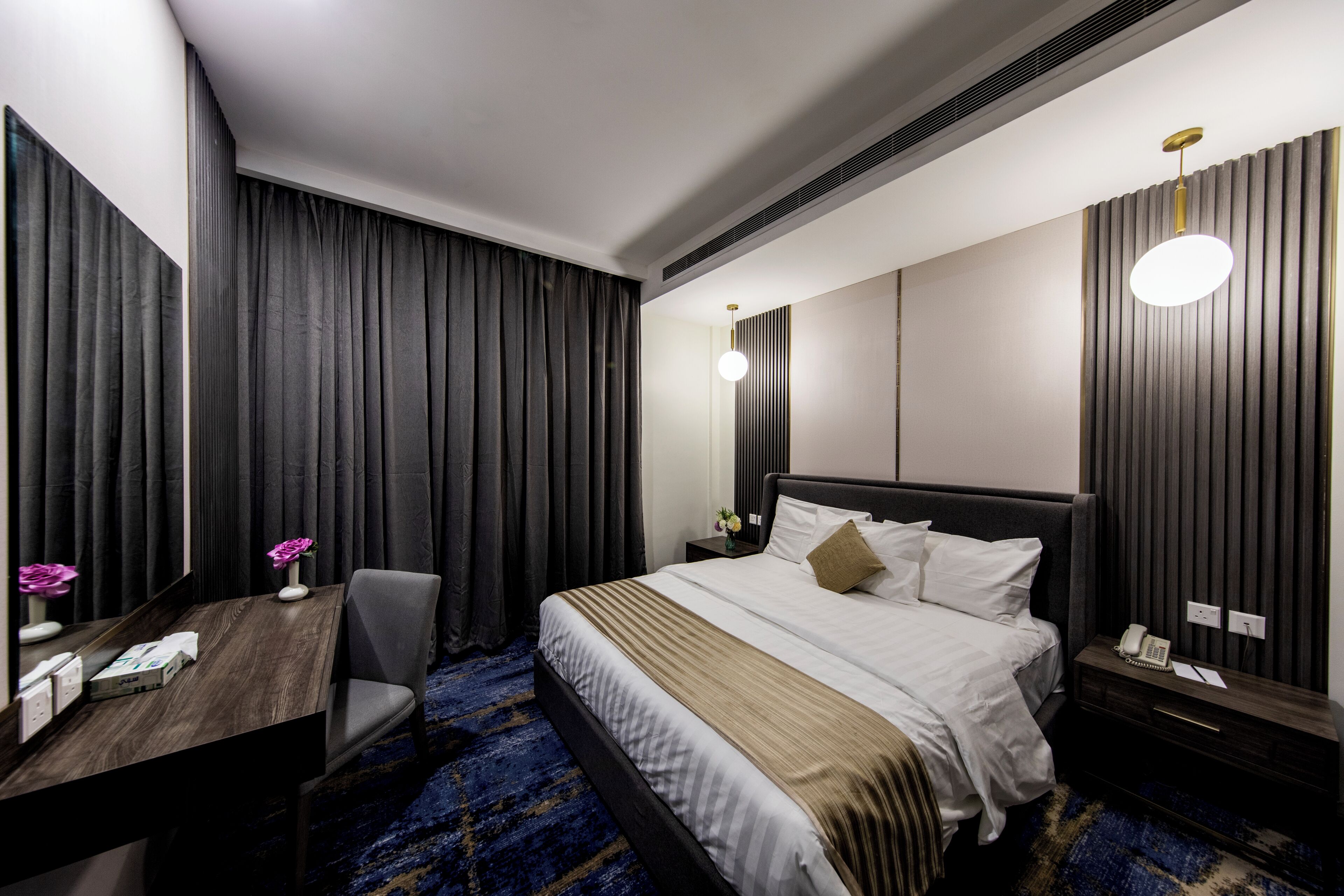 Et hotelværelse med seng, skrivebord, stol, natbord og en lampe på væggen.