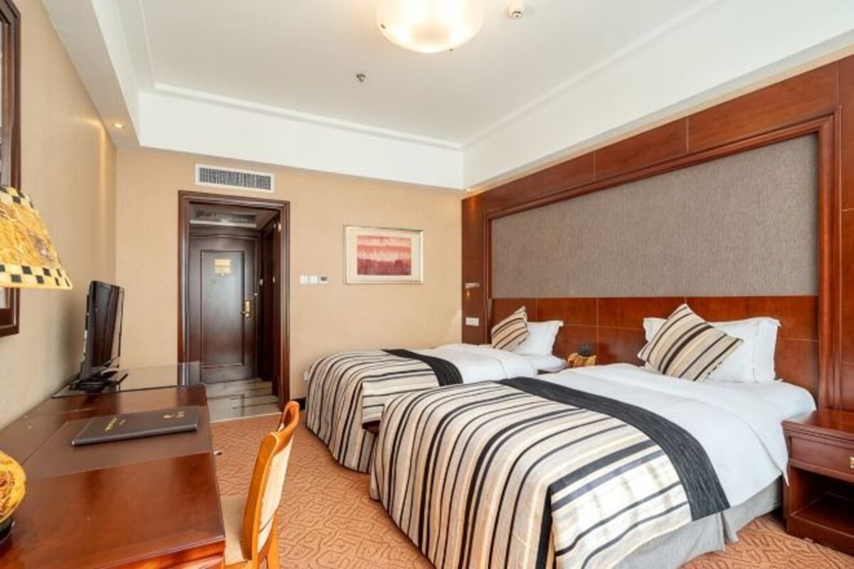 Habitación de hotel con dos camas, un escritorio, una silla, un televisor y una puerta que da a otra habitación.