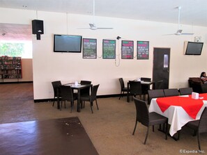 Un restaurante con varias mesas y sillas, un televisor montado en la pared y menús en una pizarra que muestran diferentes platos.