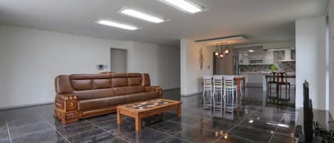 A spacious living room with a brown leather sofa, a wooden coffee table, and a kitchen in the background.