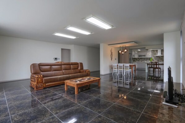 A spacious living room with a brown leather sofa, a wooden coffee table, and a kitchen in the background.