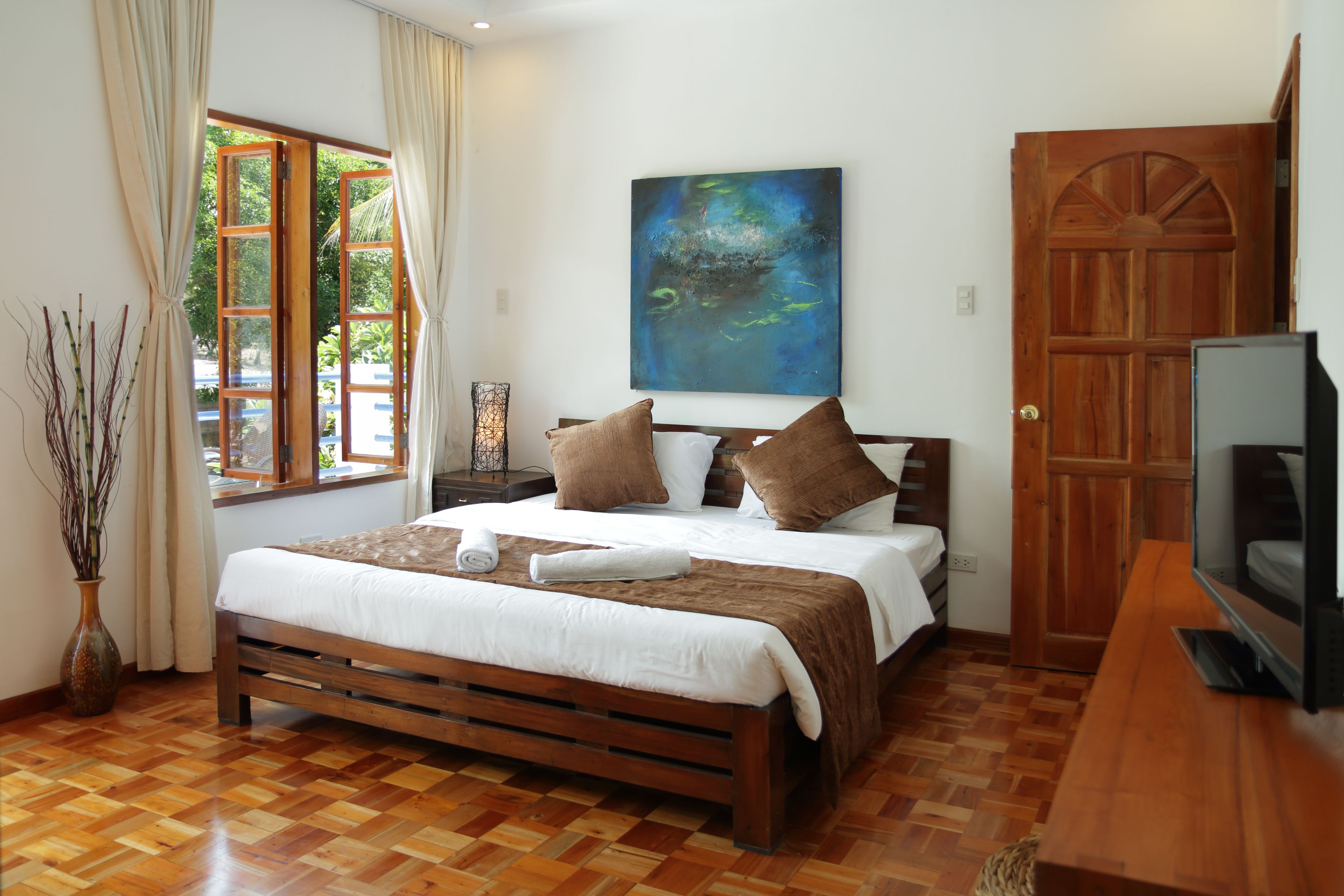 A bedroom with a wooden bed, a television, and a window with curtains.