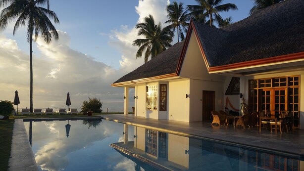 A house with a swimming pool, a patio with chairs, and a view of the ocean.