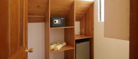 Una habitación compacta con un armario de madera que contiene una caja fuerte, un refrigerador pequeño y toallas ordenadamente dobladas.