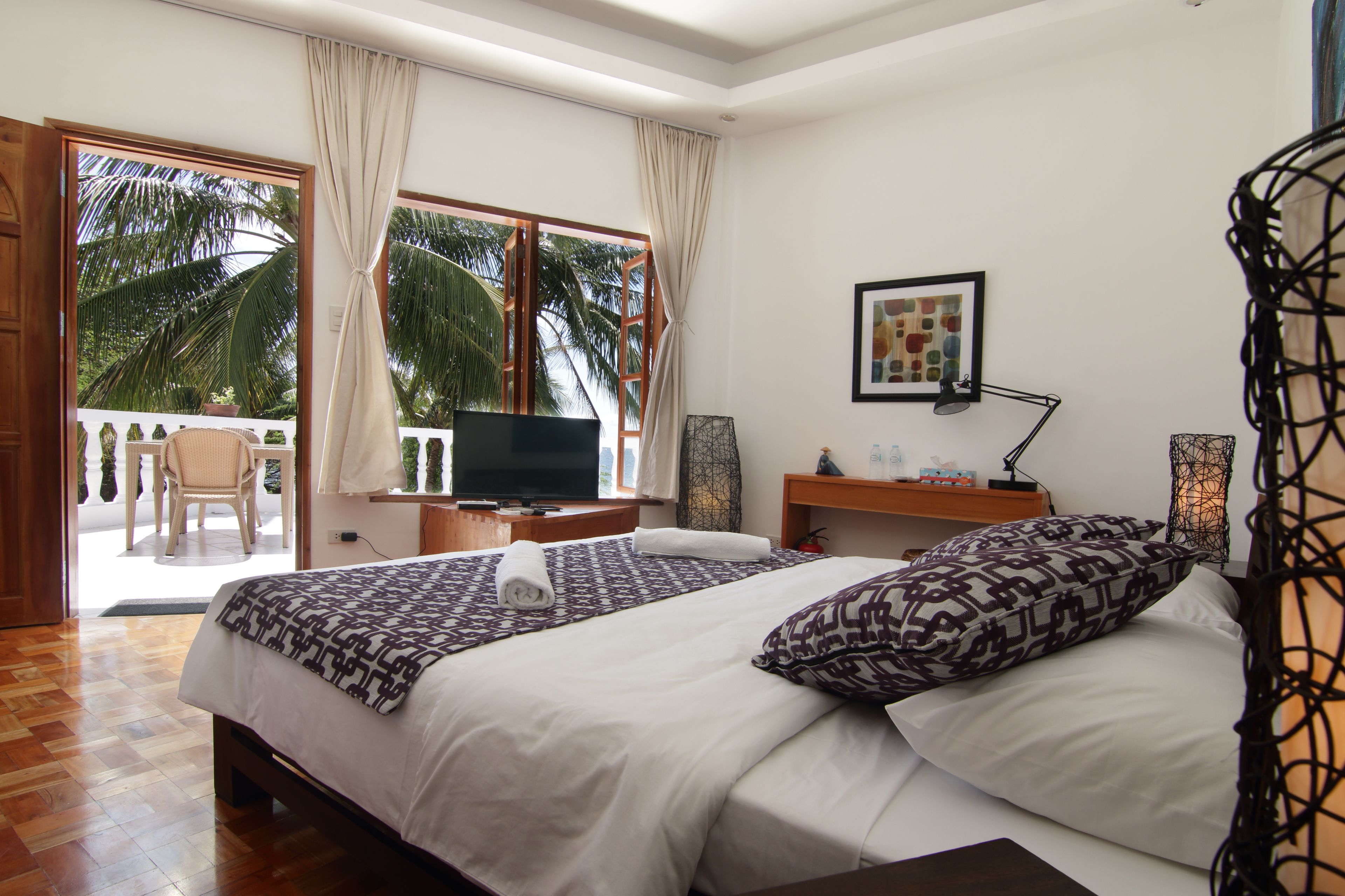Une chambre d’hôtel avec un lit, une télévision, un bureau et un balcon donnant sur des palmiers.
