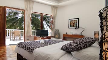 Une chambre d’hôtel avec un lit, une télévision, un bureau et un balcon donnant sur des palmiers.
