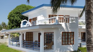 A two-story white building with a blue roof, large windows, and a balcony with blue railings.