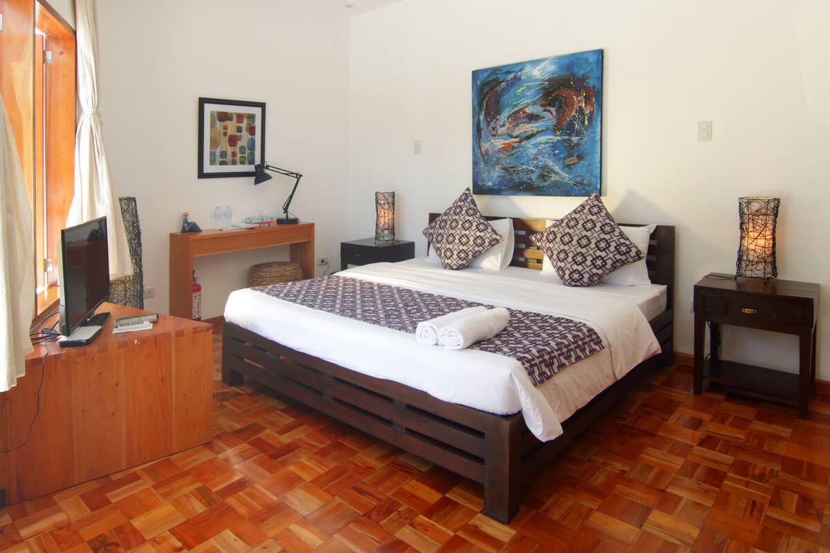 A bedroom with a wooden bed, a desk, a chair, a TV, and a painting on the wall.