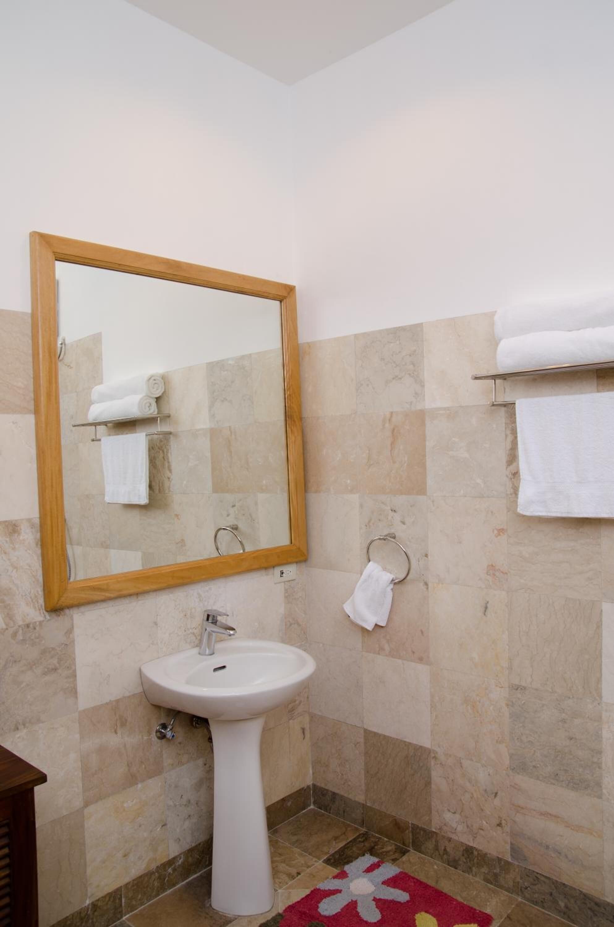Une salle de bain avec un lavabo sur colonne, un miroir avec un cadre en bois et un porte-serviettes.