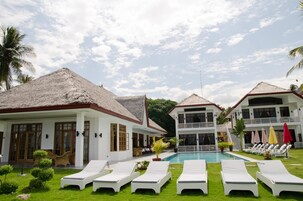 Un resort con piscina, sillones de descanso y una construcción con techo de paja.